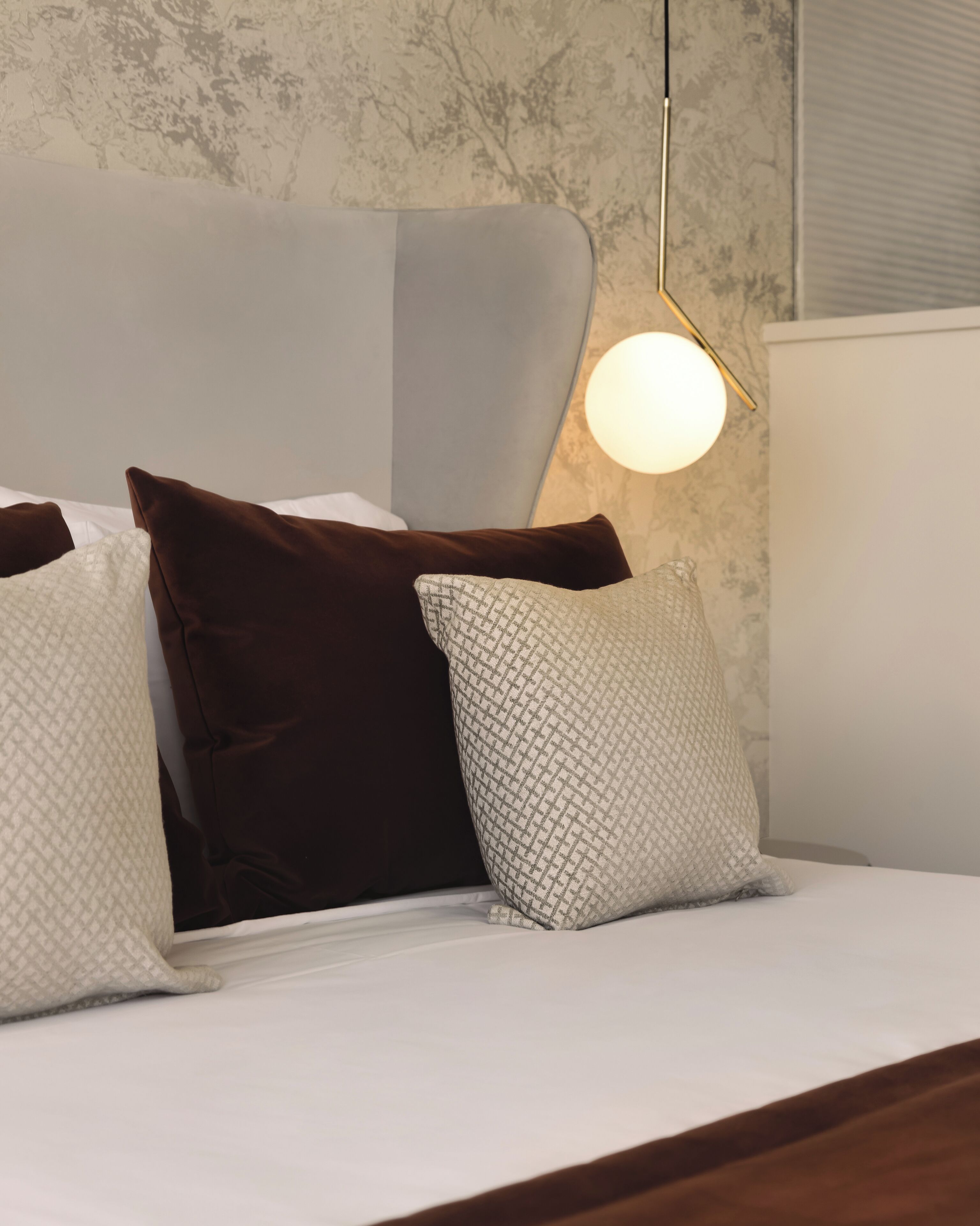 A bed with white bedding and three pillows in different patterns and colors.
