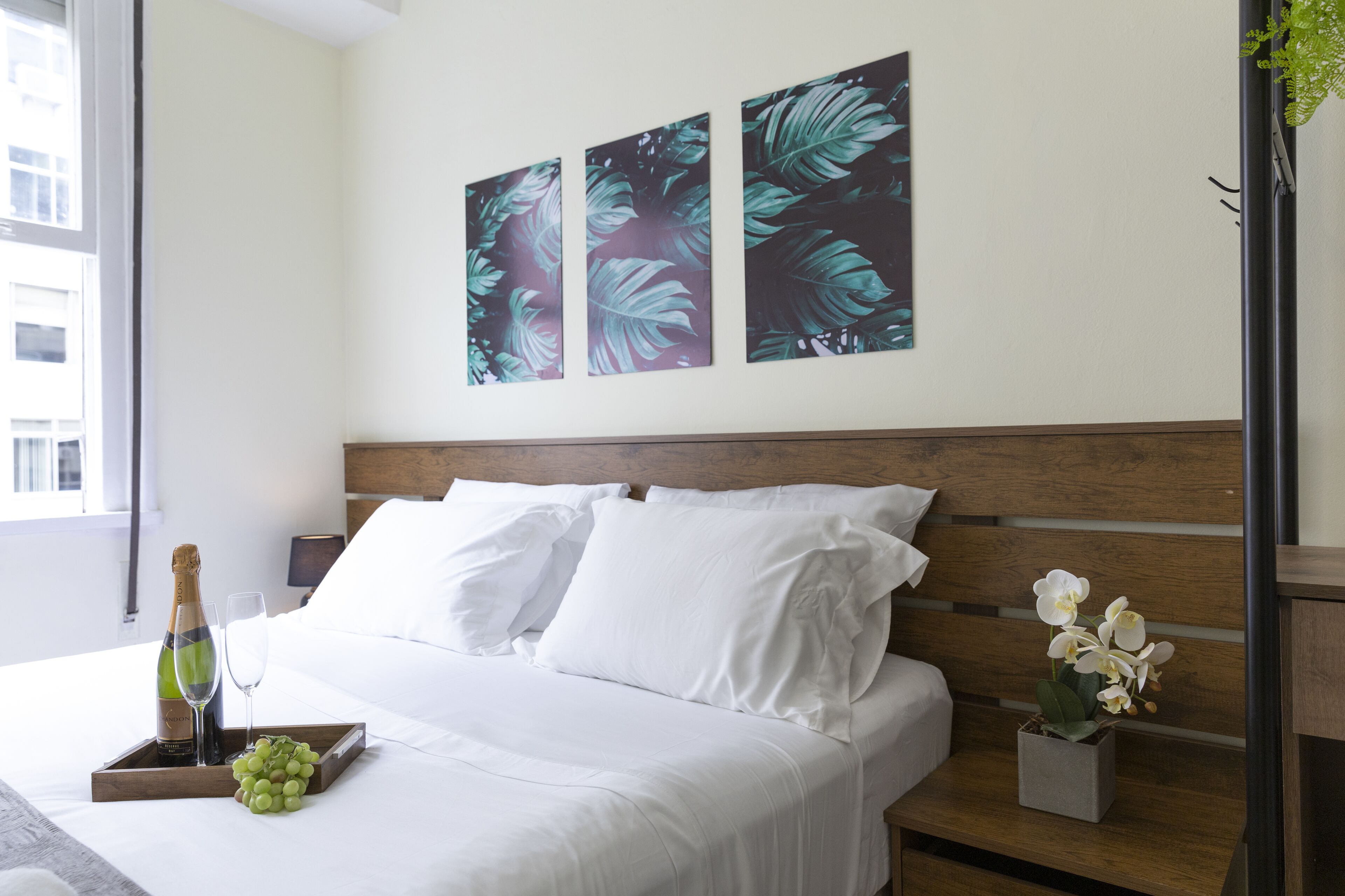 A hotel room with a bed, white linens, a bottle of champagne, a glass, and a tray with grapes.