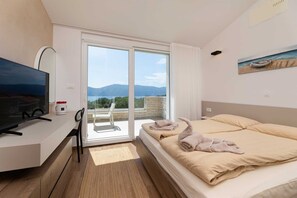 A modern hotel room with a large bed, a flat-screen TV, a desk, and a balcony with a scenic view. - Villa Olive Garden with Pool & Seaview (Brzac (Krk))