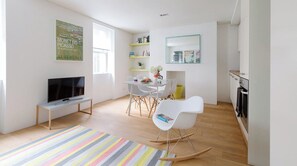 A modern living room with a flat-screen TV, a dining area with a white table and chairs, and a kitchen area with a stove and cabinets. - Fitzrovia Apartments by MoreThanStays (London)