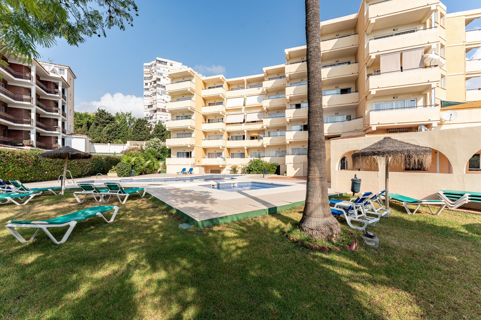 A hotel with multiple balconies, a swimming pool, and sun loungers.