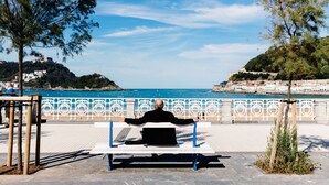 A person sitting on a bench with arms outstretched, overlooking a coastal area with a clear sky and a view of the sea. - SOUL BEACH apartment (PARKING INCLUDED) (San Sebastián/Donostia)