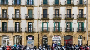 A row of parked scooters in front of a building with multiple balconies and a storefront with a sign. - SOUL BEACH apartment (PARKING INCLUDED) (San Sebastián/Donostia)
