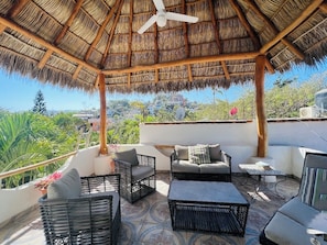 Relax on the rooftop terrace with a thatched roof, featuring wicker furniture and a scenic view.