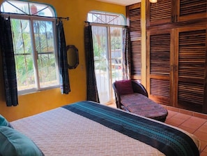 Relax in a spacious room with a large bed, a comfortable chair, and a window offering a view of palm trees.