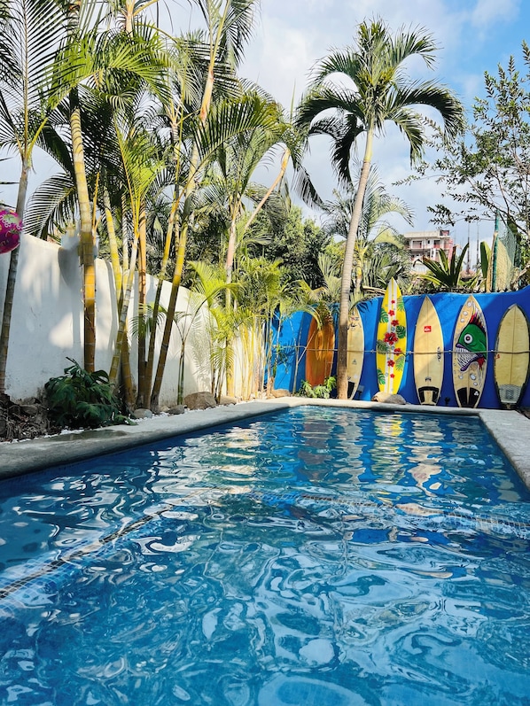 Relax by the serene pool surrounded by lush tropical vegetation and a vibrant mural.