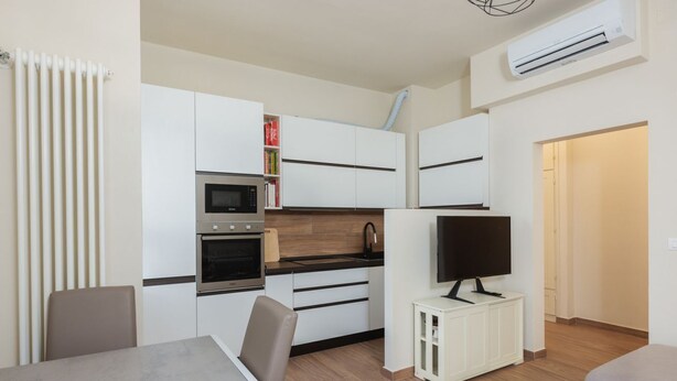 A compact kitchen with white cabinets, a microwave, oven, and a TV on a small stand. - "Ci vuole leggerezza" Apartment (Bologna)