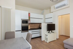 Eine kleine Küche mit weißen Schränken, einer Mikrowelle, einem Backofen und einem Fernseher auf einem kleinen Tisch.