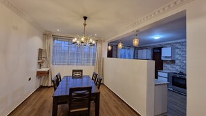 Un coin repas avec une table et des chaises en bois, un lustre et une vue sur une cuisine dont l’un des murs est en briques.