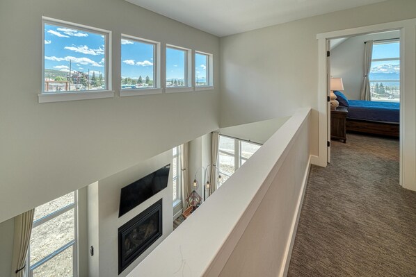 A high-ceilinged room with a fireplace, a bed with a view, and multiple windows. - Silver Vault- PET FRIENDLY-Brand New Railyard home W/ HOT TUB- minutes to Copper & Ski Cooper! (Leadville)