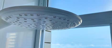 A ceiling-mounted showerhead with a circular design, a window with a view of the beach, and a tiled wall.