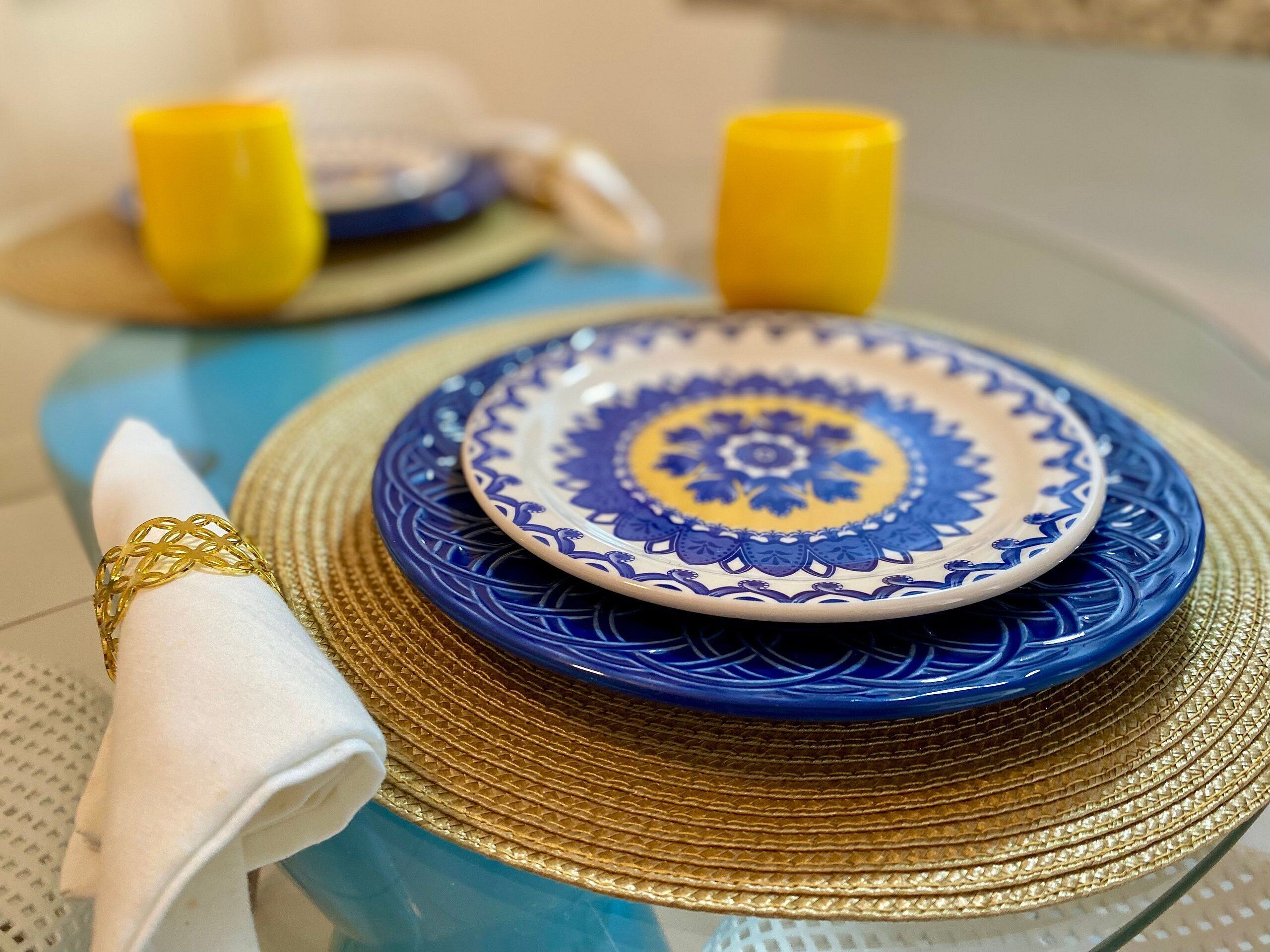 A table set with a blue and white patterned plate, a gold napkin ring, and a gold napkin.