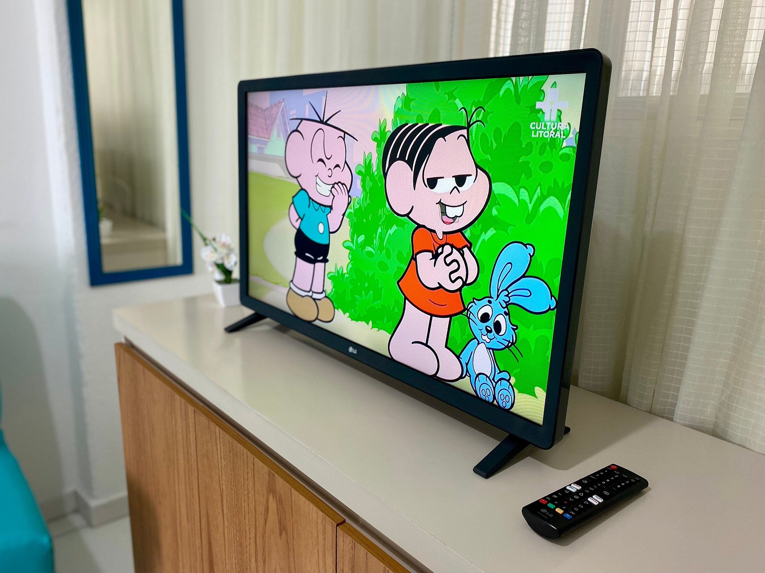 Televisão exibindo personagens animados, um controle remoto e um armário de madeira.
