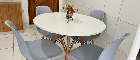A round dining table with four grey chairs, a small vase with flowers, and a wooden door in the background.