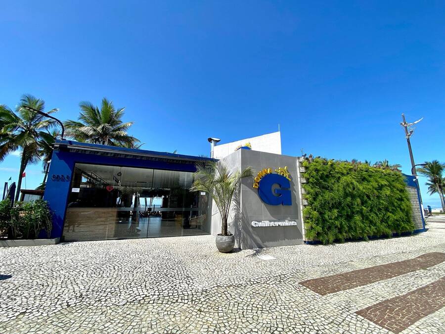 A building with a blue entrance, a sign with a large 'G', and a green hedge.
