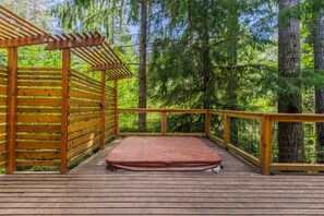 A wooden deck with a mattress, surrounded by a wooden railing and a pergola.