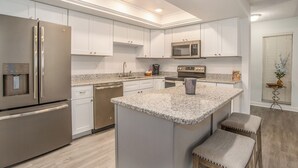 A modern kitchen with white cabinetry, stainless steel appliances, granite countertops, and a central island with stools.