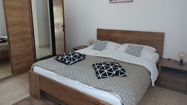 A bedroom with a wooden bed, a nightstand, a mirror, and a painting on the wall. - Studio Apartment Nikola (Janjina)