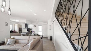 Un salon moderne avec un canapé d’angle beige, une cuisine en arrière-plan et un escalier doté d’une rampe noire.