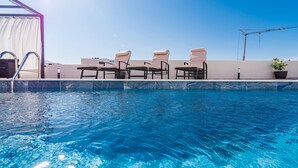 Une piscine à l’eau d’un bleu cristallin, entourée de chaises longues et d’un espace de repos abrité.