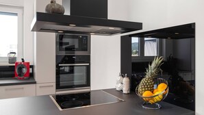 Une cuisine moderne dotée d’un four encastré, d’une hotte en acier inoxydable et d’un saladier rempli de fruits posé sur le plan de travail.
