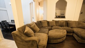 Un saló amb un sofà modular, una zona de menjador amb cadires, i una cuina al fons.