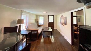 A spacious living room with a sofa, a coffee table, and a TV. There is a dining area with a table and chairs. The room has wooden flooring and white walls. - Cozy Country Home for all ATV Riders! Direct Access to Tackett and Royal Blue! (LaFollette)