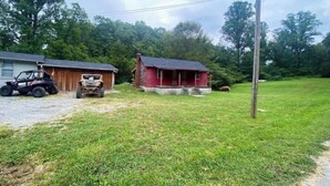 A rural property with two wooden buildings, one with a red exterior and another with a grey exterior. There is a dirt path leading to the buildings, and a utility pole is visible in the background. - Cozy Country Home for all ATV Riders! Direct Access to Tackett and Royal Blue! (LaFollette)
