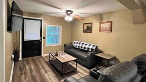 Un salon avec un canapé en cuir noir, une table basse, un ventilateur de plafond et deux tableaux encadrés accrochés au mur.