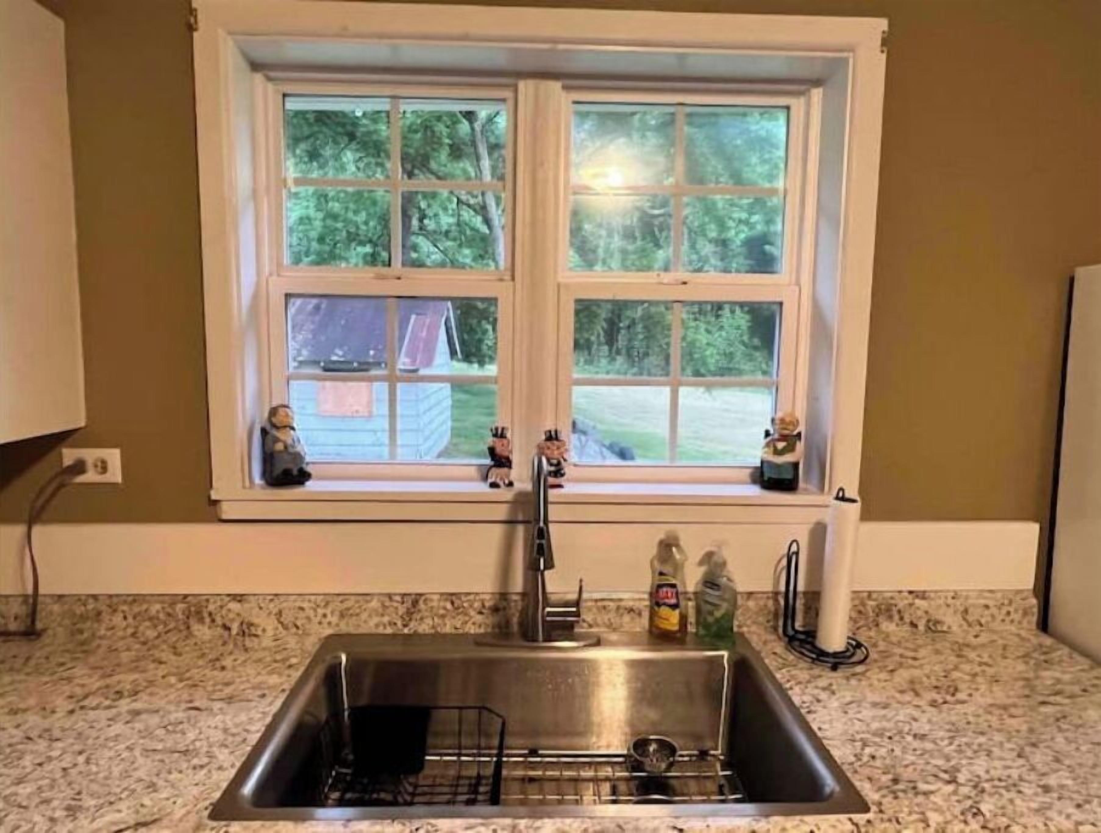 A kitchen with a double sink, a window above it, and a view of a house and trees outside.