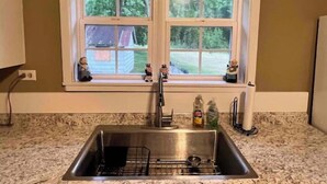 Une cuisine équipée d’un évier à deux bacs, avec une fenêtre au-dessus, et donnant sur une maison et des arbres à l’extérieur.