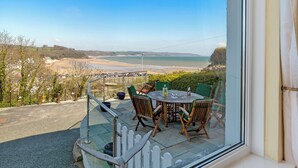 A terrace with a table and chairs overlooking a beach and distant landscape. - White Sails - Beach and Harbour Views (Saundersfoot)
