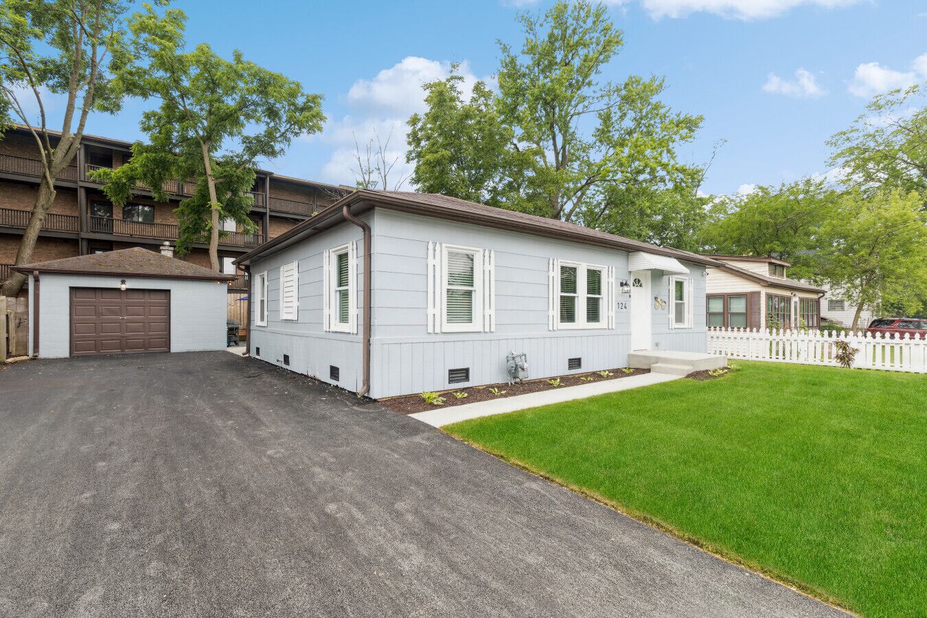 A single-story house with a garage, a front yard, and a white picket fence.
