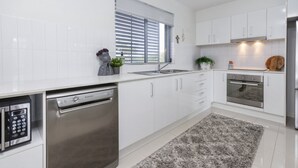 A modern kitchen with white cabinetry, stainless steel appliances, and a grey rug. - Modern Beachside Escape (WOORIM)