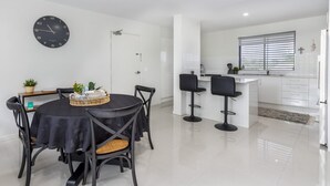 A modern kitchen with white cabinets, a black clock, and a dining area with a round table and chairs. - Modern Beachside Escape (WOORIM)