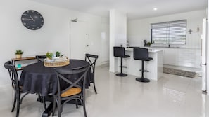 A modern kitchen with white cabinets, a black clock, and a dining area with a round table and chairs.