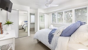 A bedroom with a bed, a TV, a desk, and a window with blinds. - Modern Beachside Escape (WOORIM)