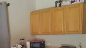 Una cocina con armarios de madera, microondas, licuadora y refrigerador.