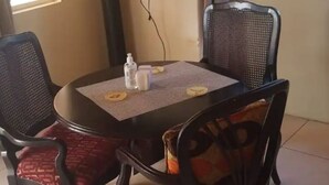 Un comedor con una mesa redonda, cuatro sillas, un televisor de pantalla plana montado en la pared y una ventana con cortinas.