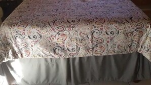 Una cama con una colcha estampada, una toalla blanca y una almohada roja.