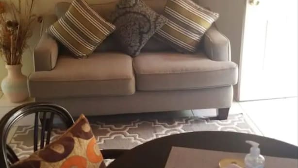 Una sala de estar con sofá, cojines estampados, una mesita de centro con posavasos y un florero con plantas secas.