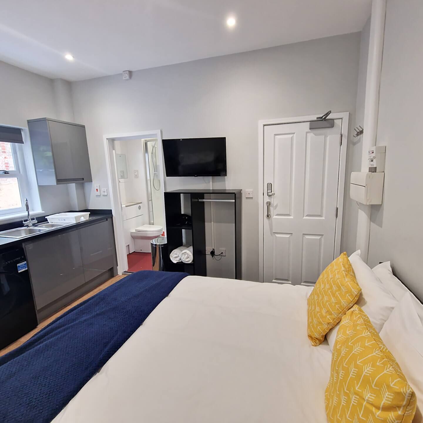 A hotel room with a bed, a TV, a wardrobe, a bathroom, and a kitchenette.