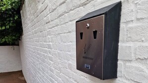 Eine Metallschachtel mit dem Aufdruck "SMOKERS STATION" an einer weißen Ziegelwand angebracht.
