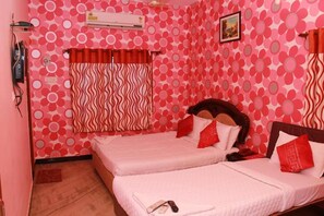 A room with two beds, a patterned wall, an air conditioner, and a window with curtains.