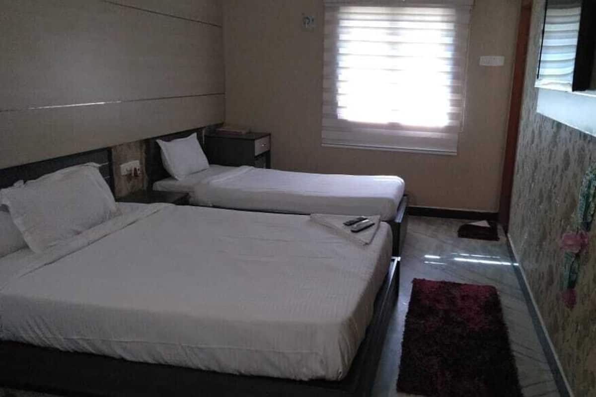 Een hotelkamer met twee bedden, een klein raam met zonwering, een nachtkastje en een rood tapijt.