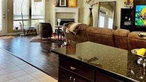 A spacious living room with a fireplace, a large sofa, a dining area, and a kitchen with dark cabinetry. - South Austin gem - Kickback and relax! (Manchaca)