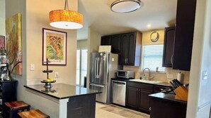A modern kitchen with dark cabinetry, stainless steel appliances, and a central island with stools. - South Austin gem - Kickback and relax! (Manchaca)