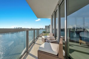 A balcony with wicker furniture, a glass railing, and a view of the water and city skyline. - Stunning 2BR 2BA  Bay Harbour with Pool (Bay Harbor Islands)