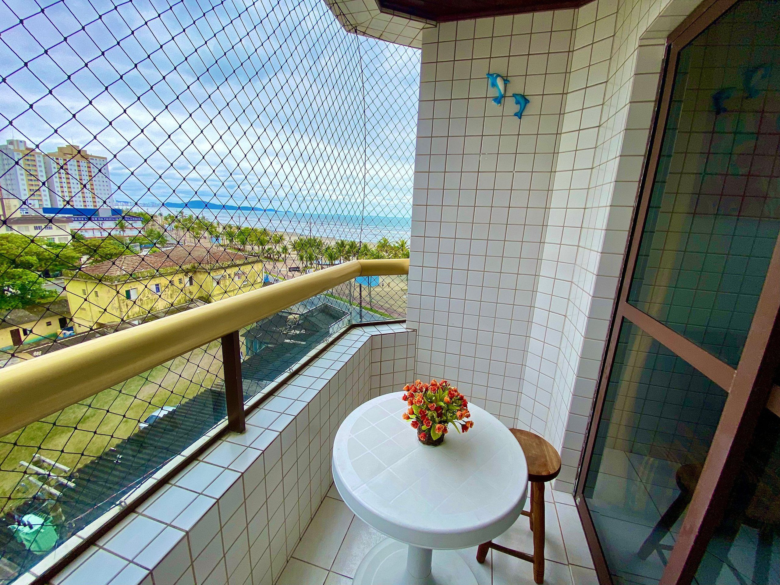 A balcony with a white table and a flower vase, a tiled wall, and a view of buildings and a body of water.
