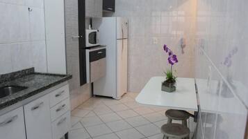 Une cuisine compacte avec un réfrigérateur blanc, un four à micro-ondes et une petite table avec des tabourets.